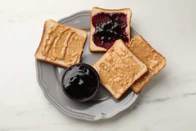 Photo of Delicious toasts with peanut butter and jam on white marble table, top view