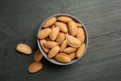 Photo of Ceramic bowl with almonds on black table, flat lay. Cooking utensil