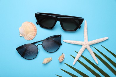 Stylish sunglasses, starfish and seashells on light blue background, flat lay