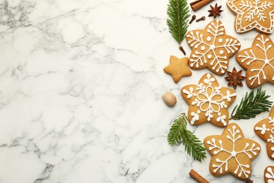 Photo of Tasty star shaped Christmas cookies with icing, spices and fir tree twigs on white marble table, flat lay. Space for text