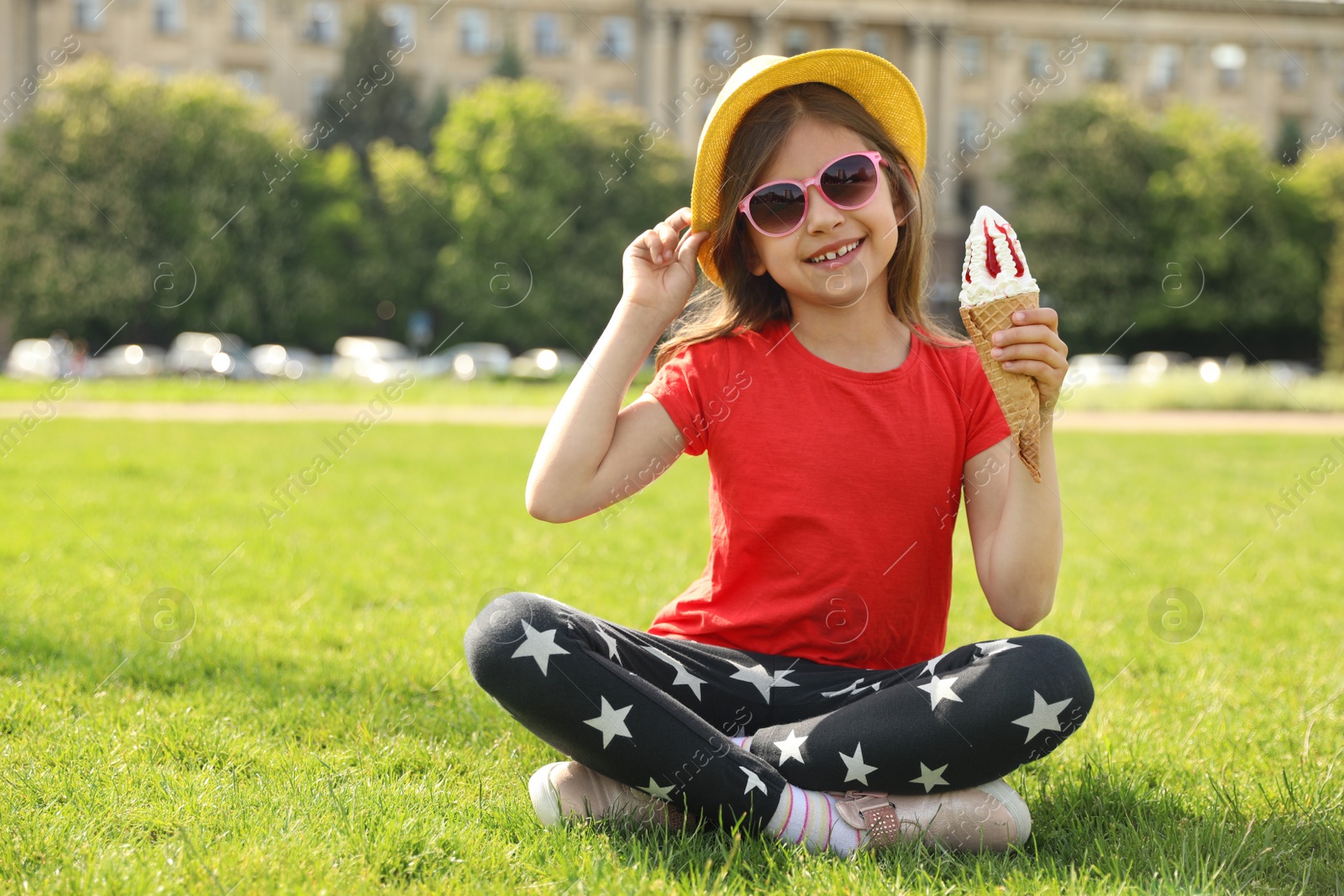 Photo of Cute little girl with delicious ice cream sitting on green grass outdoors