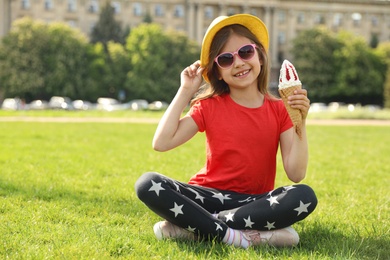 Cute little girl with delicious ice cream sitting on green grass outdoors