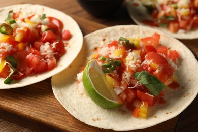 Photo of Delicious tacos with vegetables, lime and ketchup on wooden table, closeup