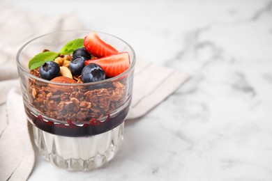 Photo of Tasty granola with berries, nuts, jam and yogurt in glass on white marble table, closeup. Space for text