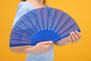 Woman holding hand fan on orange background, closeup