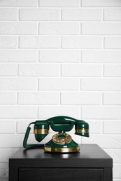 Green vintage corded phone on small black table near white brick wall. Space for text