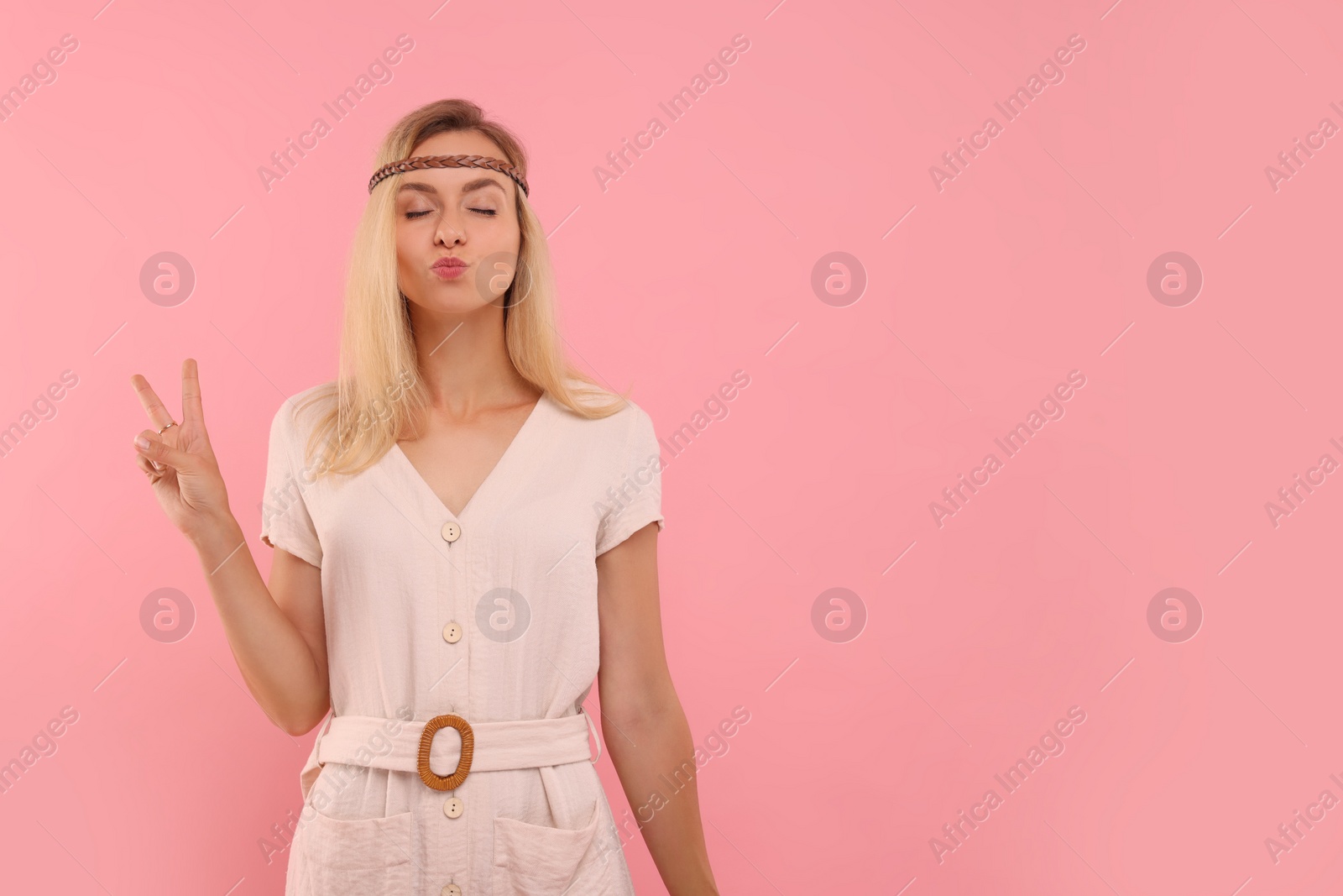 Photo of Portrait of hippie woman showing peace sign on pink background. Space for text