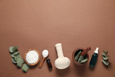 Different aromatherapy products, mortar and eucalyptus leaves on brown background, flat lay. Space for text