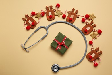 Greeting card for doctor with stethoscope, gift box and Christmas decor on beige background, flat lay