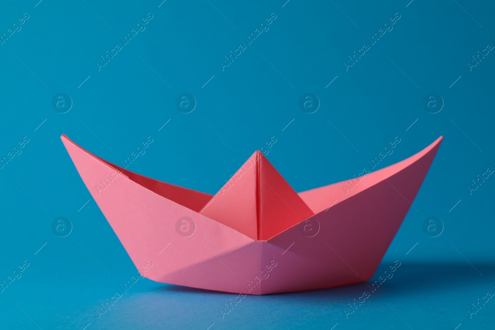 Photo of Handmade pink paper boat on light blue background. Origami art