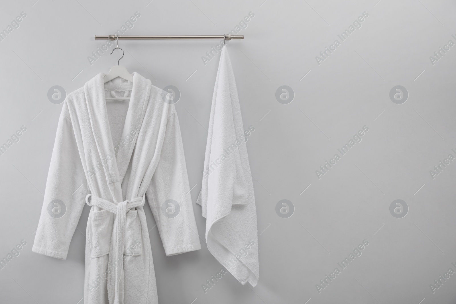 Photo of Hanger with clean bathrobe and towel on light wall. Space for text