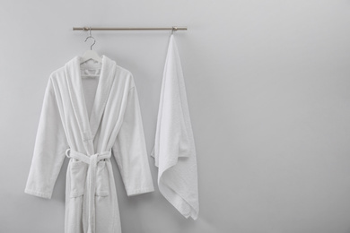 Photo of Hanger with clean bathrobe and towel on light wall. Space for text