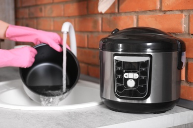 Photo of Woman washing modern multi cooker in kitchen sink, selective focus