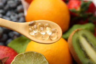 Photo of Vitamin pills in spoon over fresh fruits, closeup