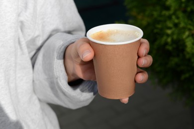 Photo of Woman holding cardboard cup with coffee outdoors, closeup