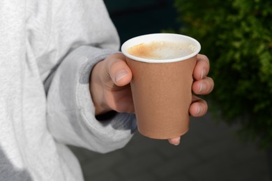 Woman holding cardboard cup with coffee outdoors, closeup