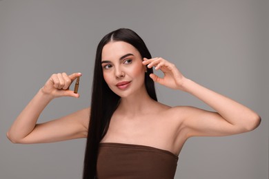 Photo of Beautiful young woman holding skincare ampoule on grey background