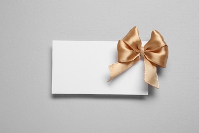Photo of Blank gift card with golden bow on light grey background, top view. Space for text