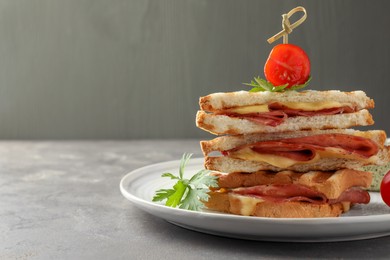 Stack of tasty sandwiches with ham and melted cheese served with tomato on grey textured table, closeup. Space for text
