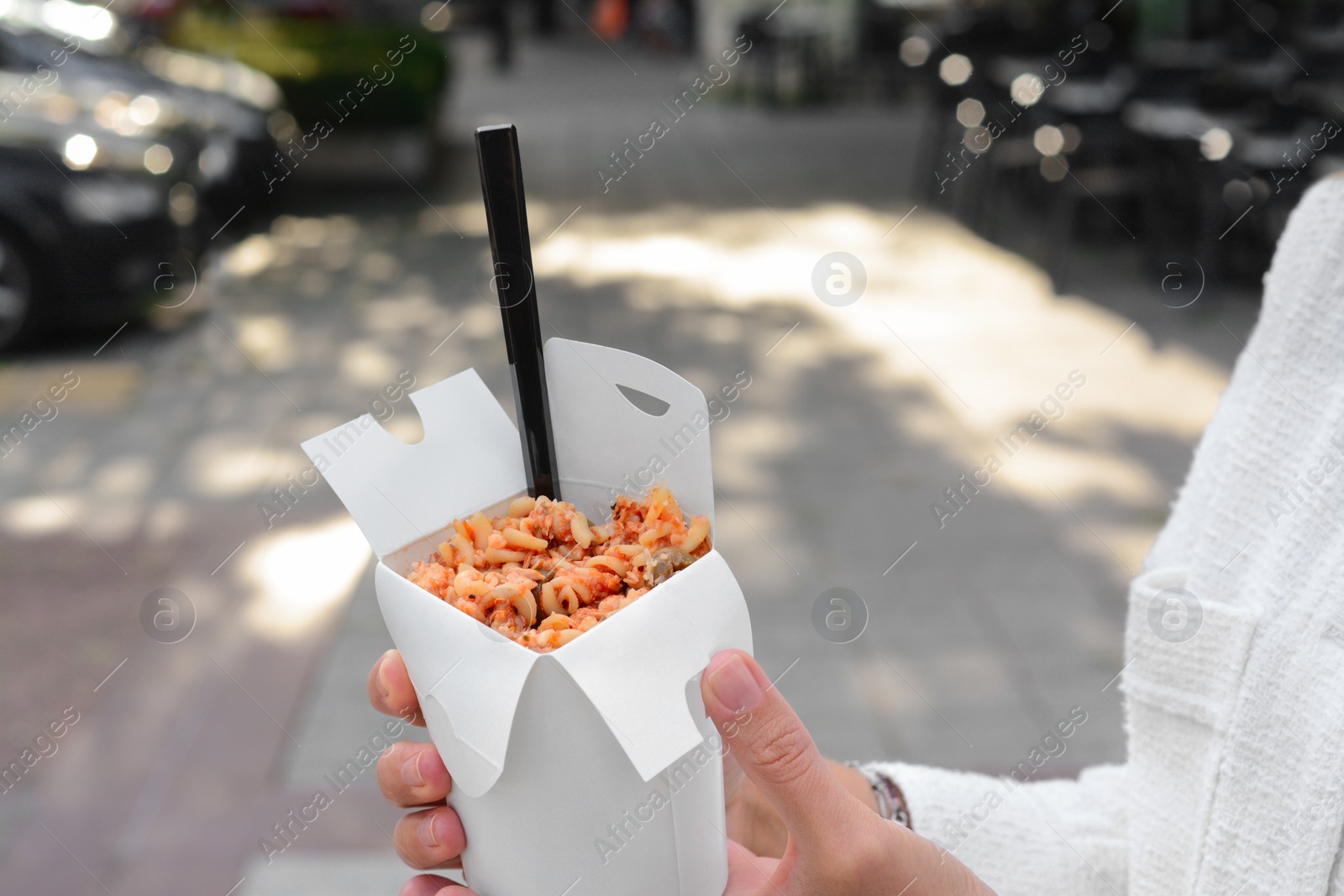 Photo of Woman holding paper box of takeaway noodles with fork outdoors, closeup. Street food