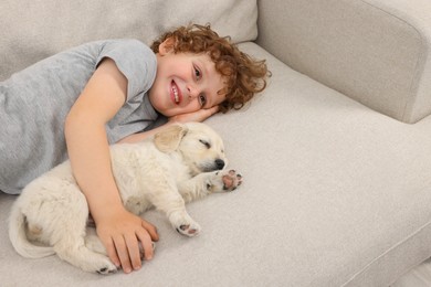 Photo of Little boy hugging cute puppy on couch. Space for text