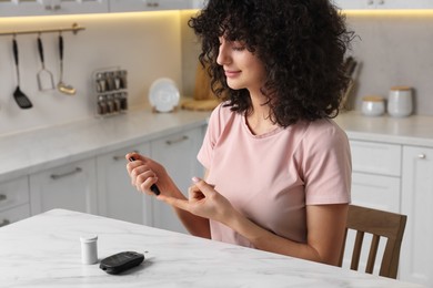 Diabetes. Woman using lancet pen at white marble table in kitchen