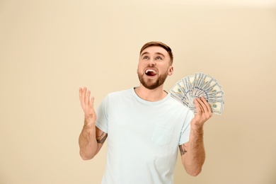 Portrait of emotional young man with money on color background