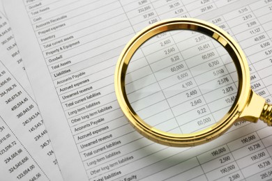 Photo of Looking on accounting documents through magnifying glass, closeup