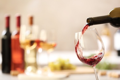 Pouring red wine from bottle into glass on blurred background. Space for text