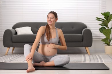 Pregnant woman sitting on yoga mat at home