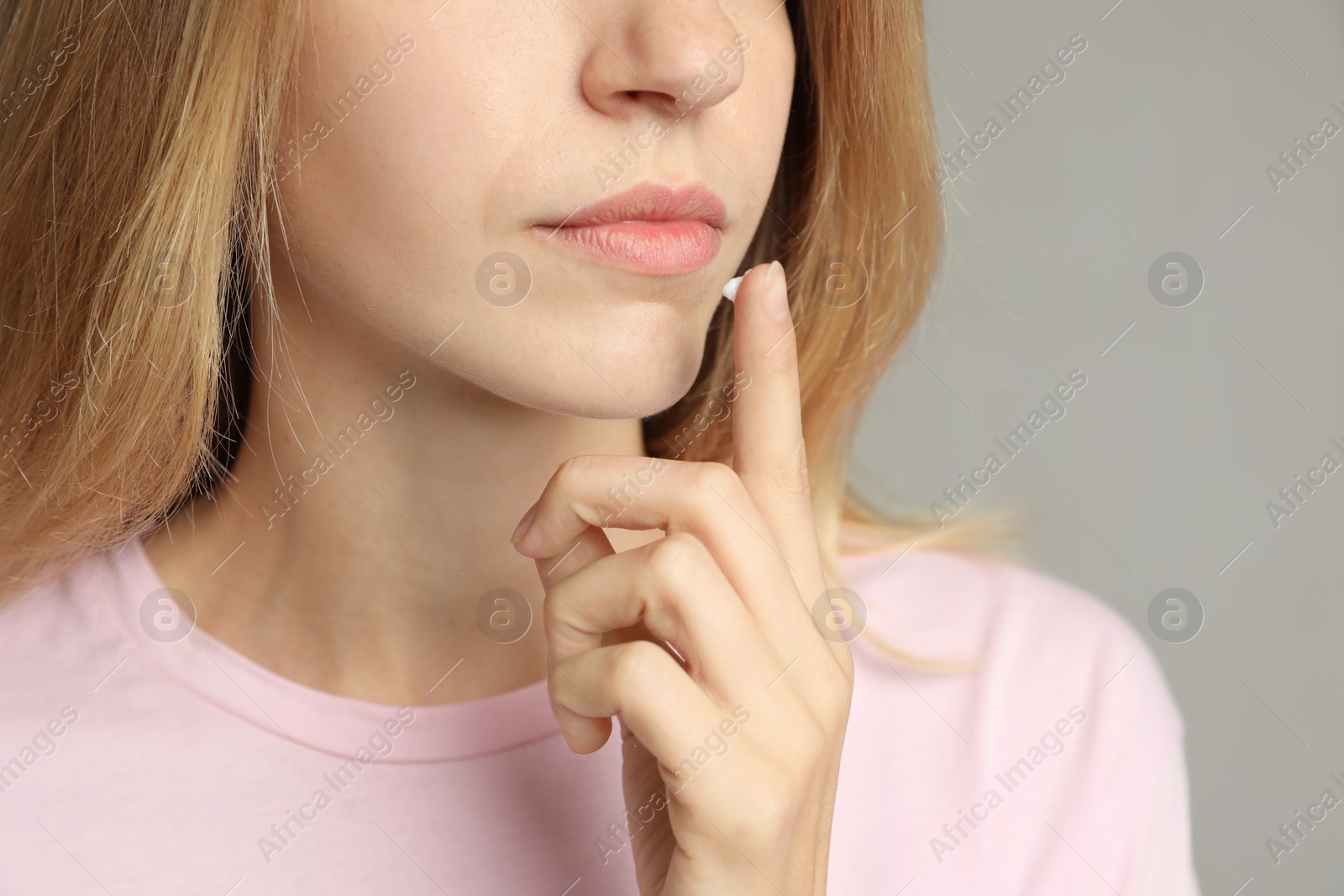 Photo of Woman with herpes applying cream onto lip against light grey background, closeup