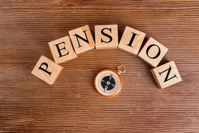 Photo of Cubes with space for text and compass on wooden background. Pension planning