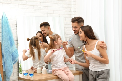 Photo of Little girl and her parents brushing teeth together in bathroom at home. Space for text