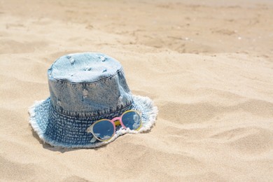 Jeans hat and sunglasses on sand, space for text. Beach accessories