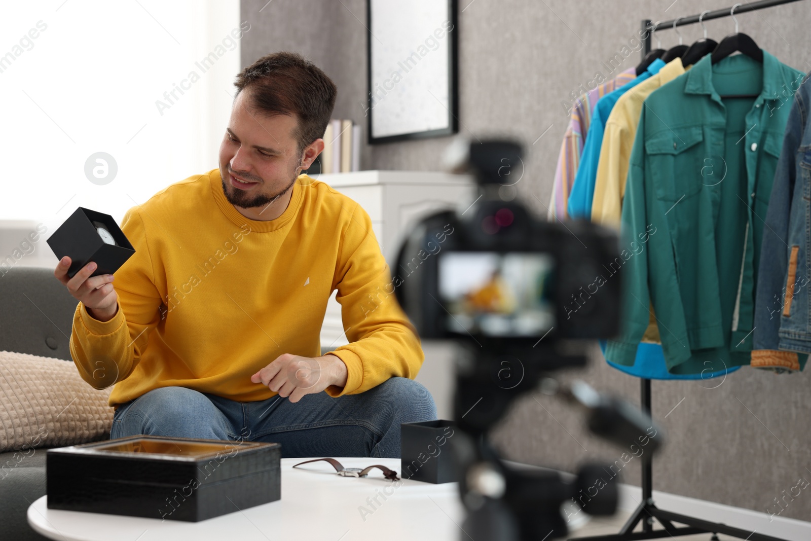 Photo of Smiling fashion blogger showing wristwatches while recording video at home