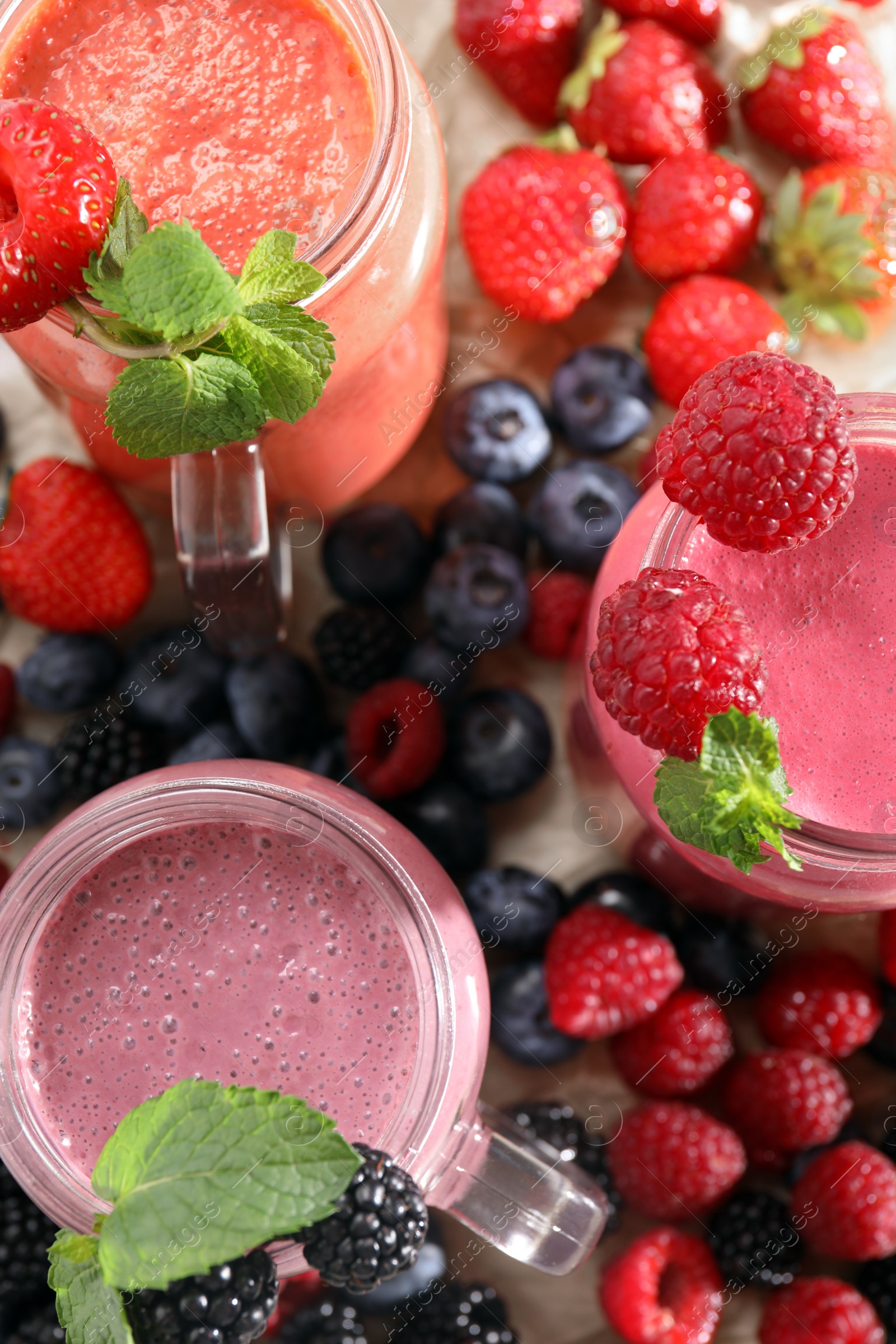 Photo of Mason jars of different berry smoothies and fresh ingredients on wooden table, top view