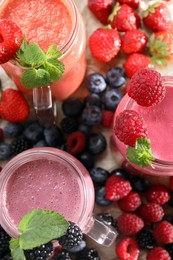 Mason jars of different berry smoothies and fresh ingredients on wooden table, top view