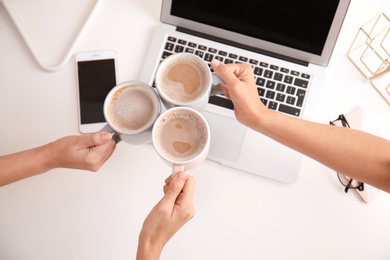 Photo of Women holding coffee cups at modern workplace in office, top view