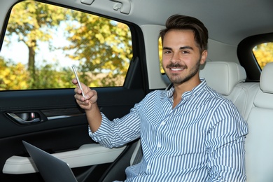 Photo of Young handsome man with laptop using phone in car