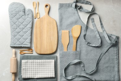Photo of Kitchen napkins, apron and different utensils on light grey table, flat lay
