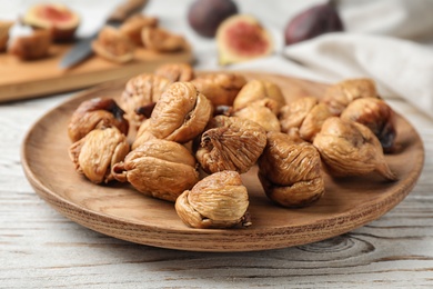 Wooden plate with tasty dried figs on white table, closeup