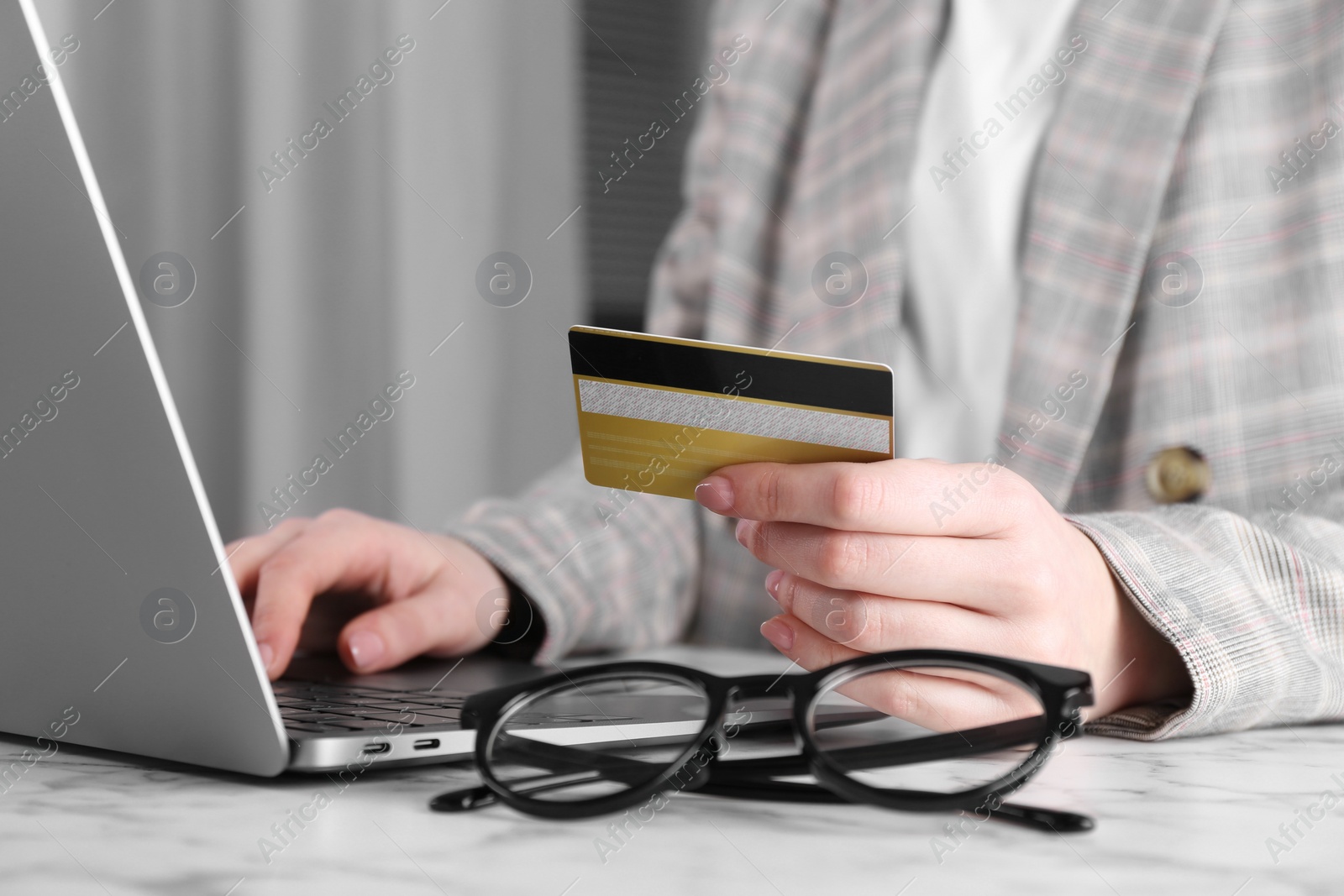 Photo of Online payment. Woman with laptop and credit card at white marble table, closeup