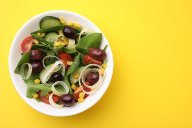 Bowl of tasty salad with leek and olives on yellow table, top view. Space for text