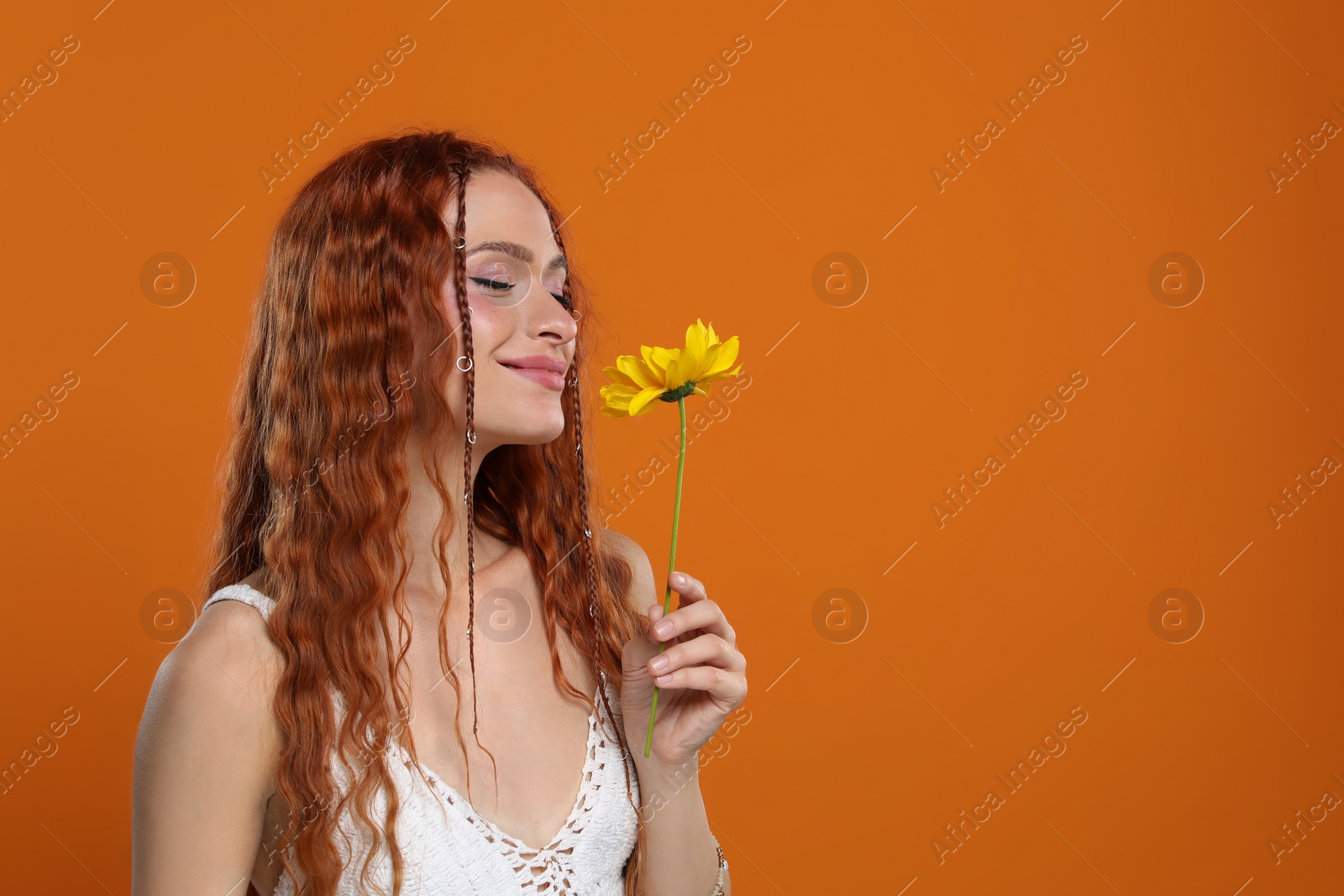 Photo of Beautiful young hippie woman with sunflower on orange background, space for text