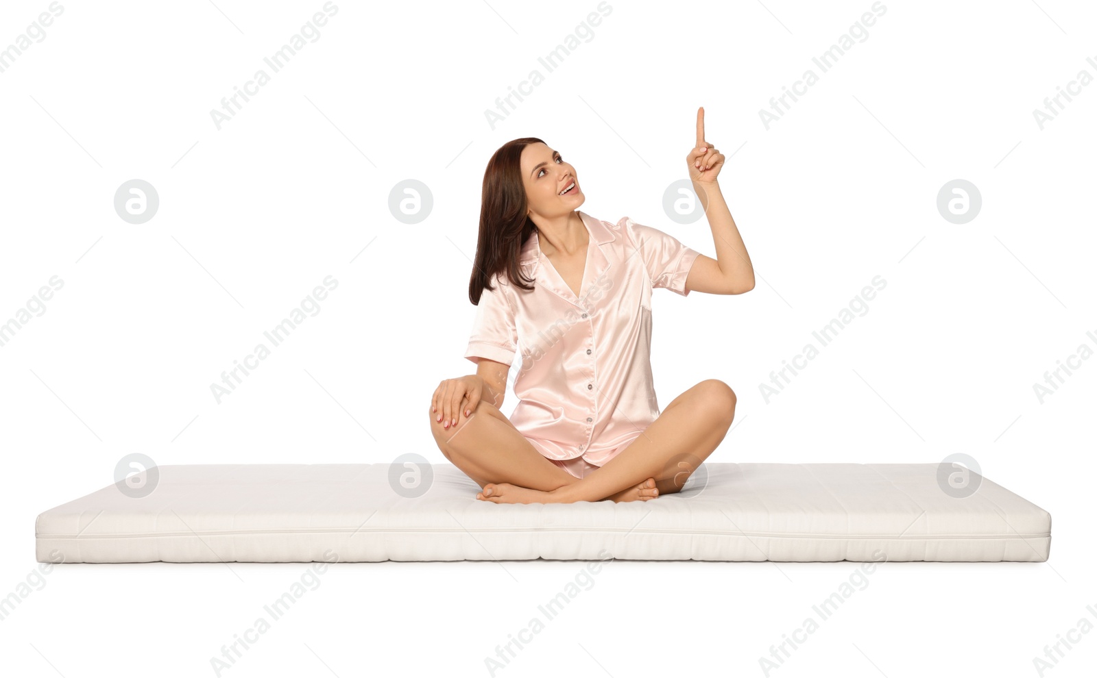 Photo of Young woman sitting on soft mattress and pointing upwards against white background