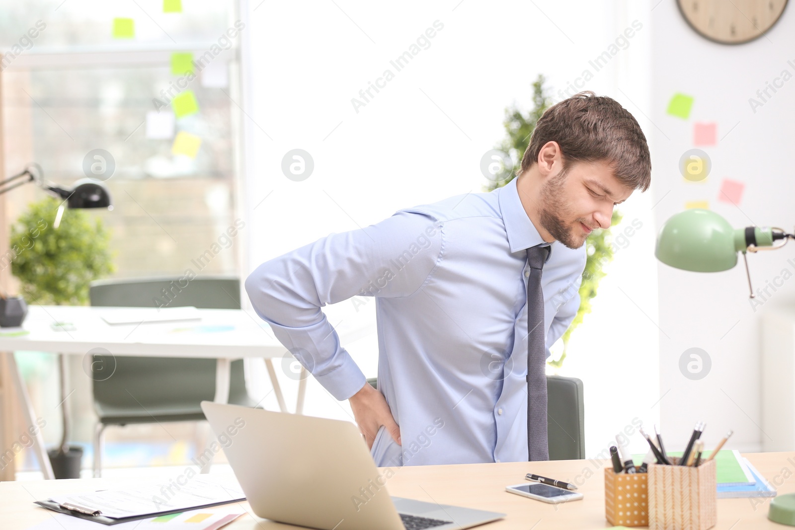 Photo of Young man suffering from back pain in office