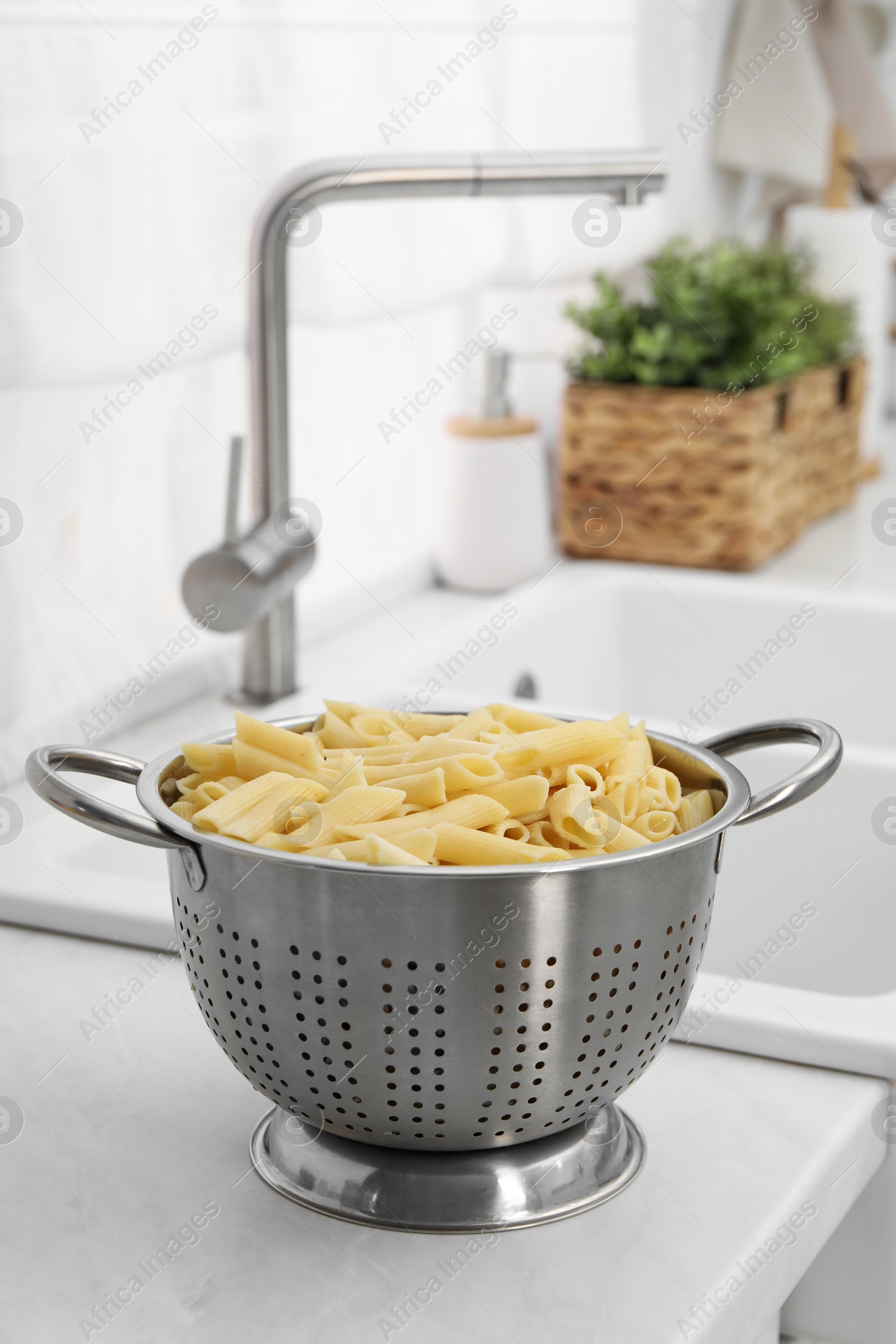 Photo of Cooked pasta in metal colander on countertop near sink. Space for text