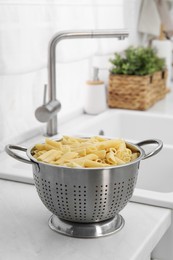 Photo of Cooked pasta in metal colander on countertop near sink. Space for text