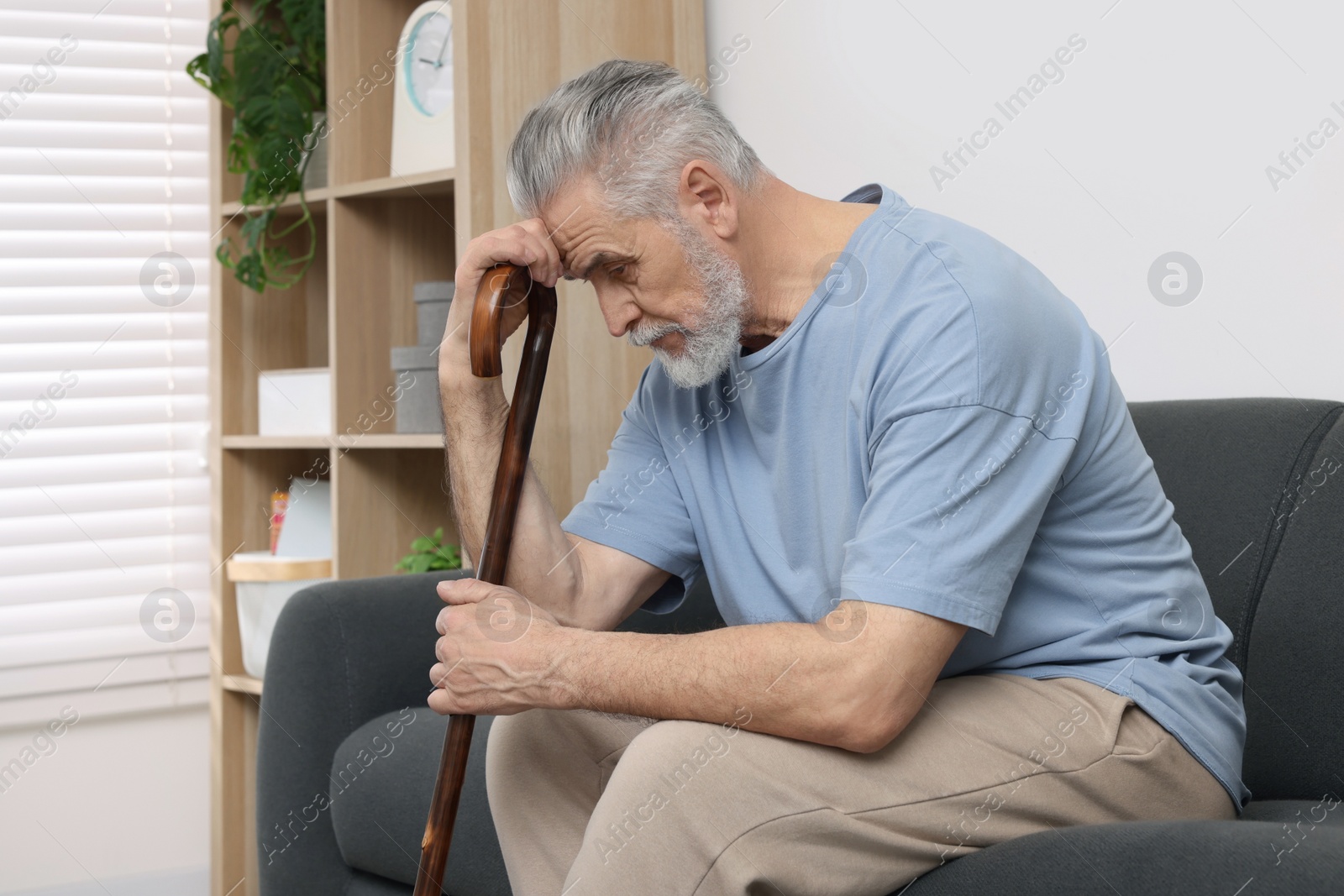 Photo of Senior man with walking cane sitting on sofa at home