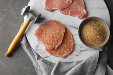 Photo of Cooking schnitzel. Raw pork chops, bread crumbs and meat mallet on grey table, top view